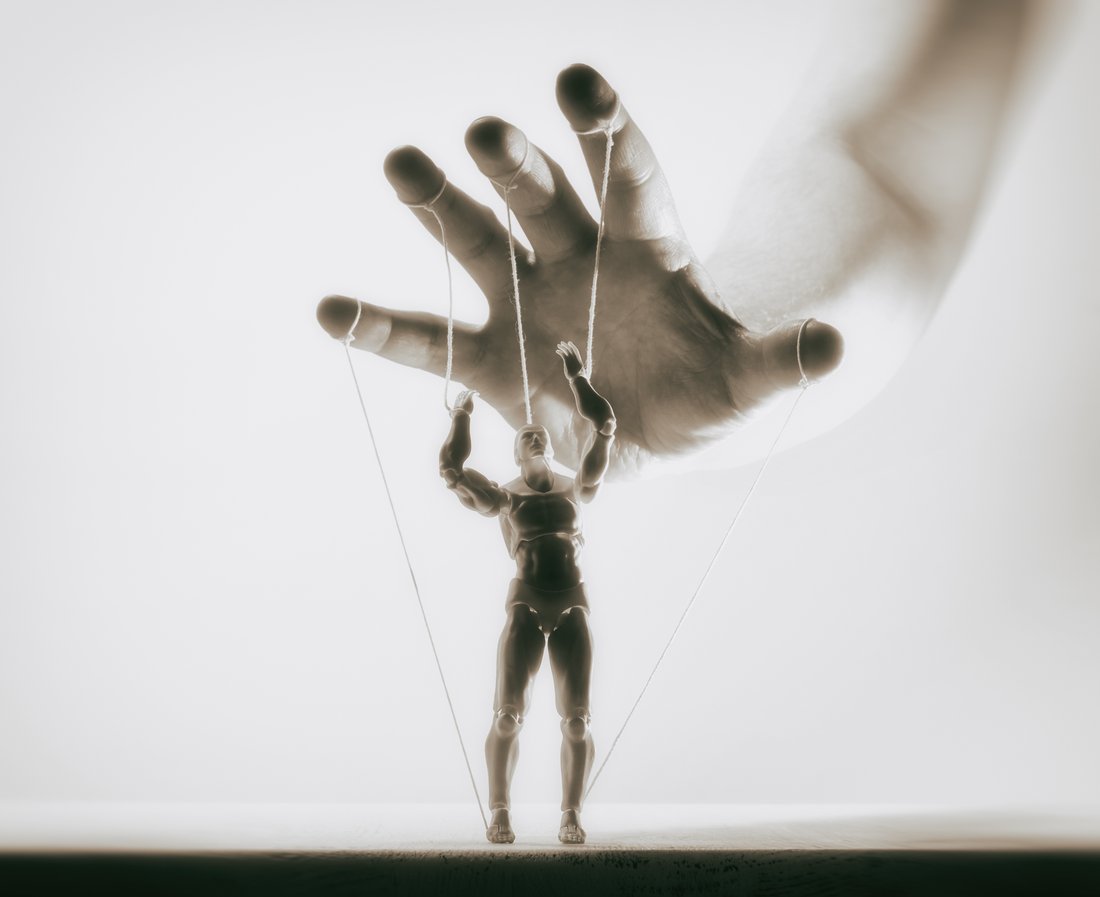 A close-up photo of a marionette figure being controlled by strings attached to an unseen puppeteer's hand above it